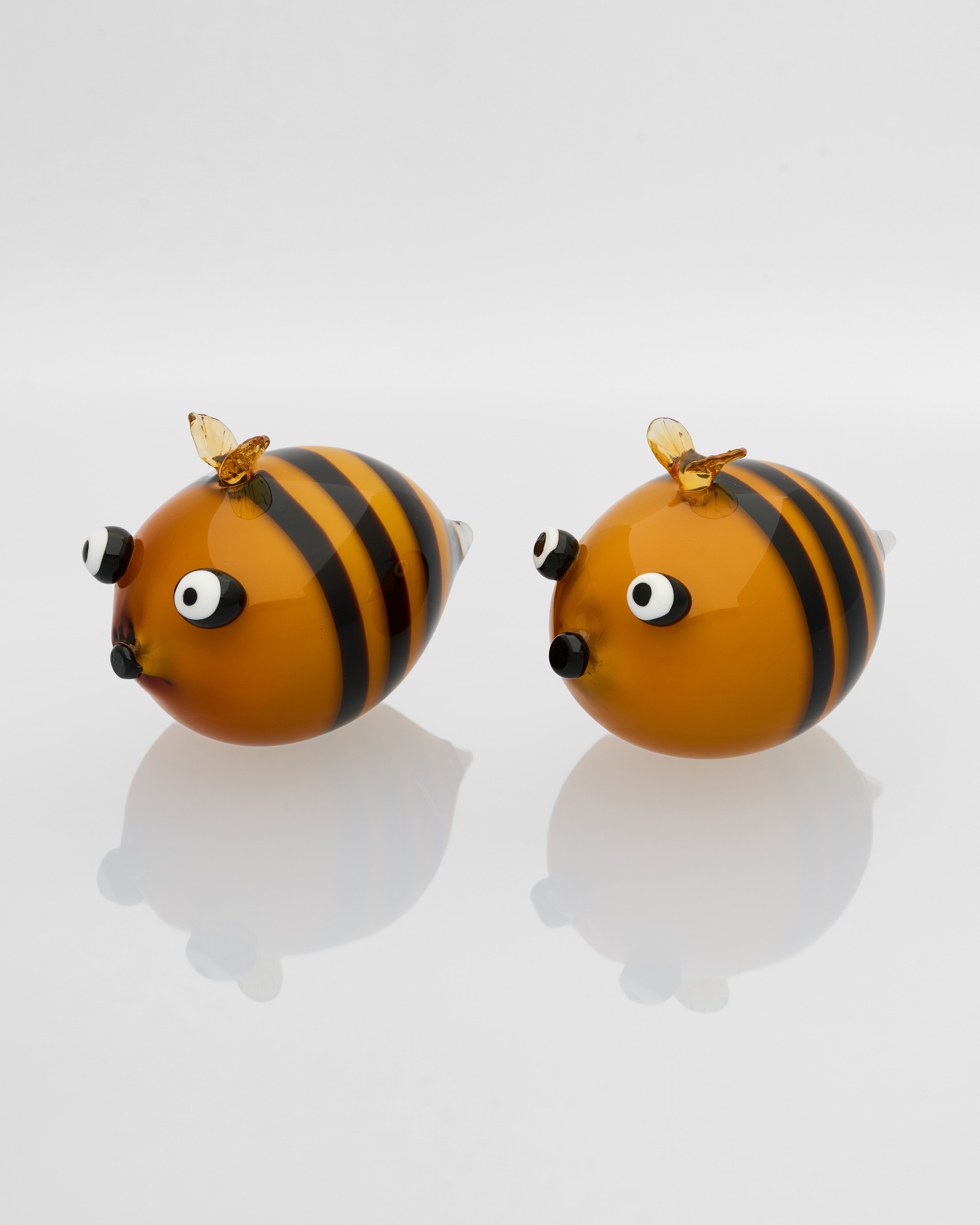 Two bee-shaped earrings on a reflective surface with a white background