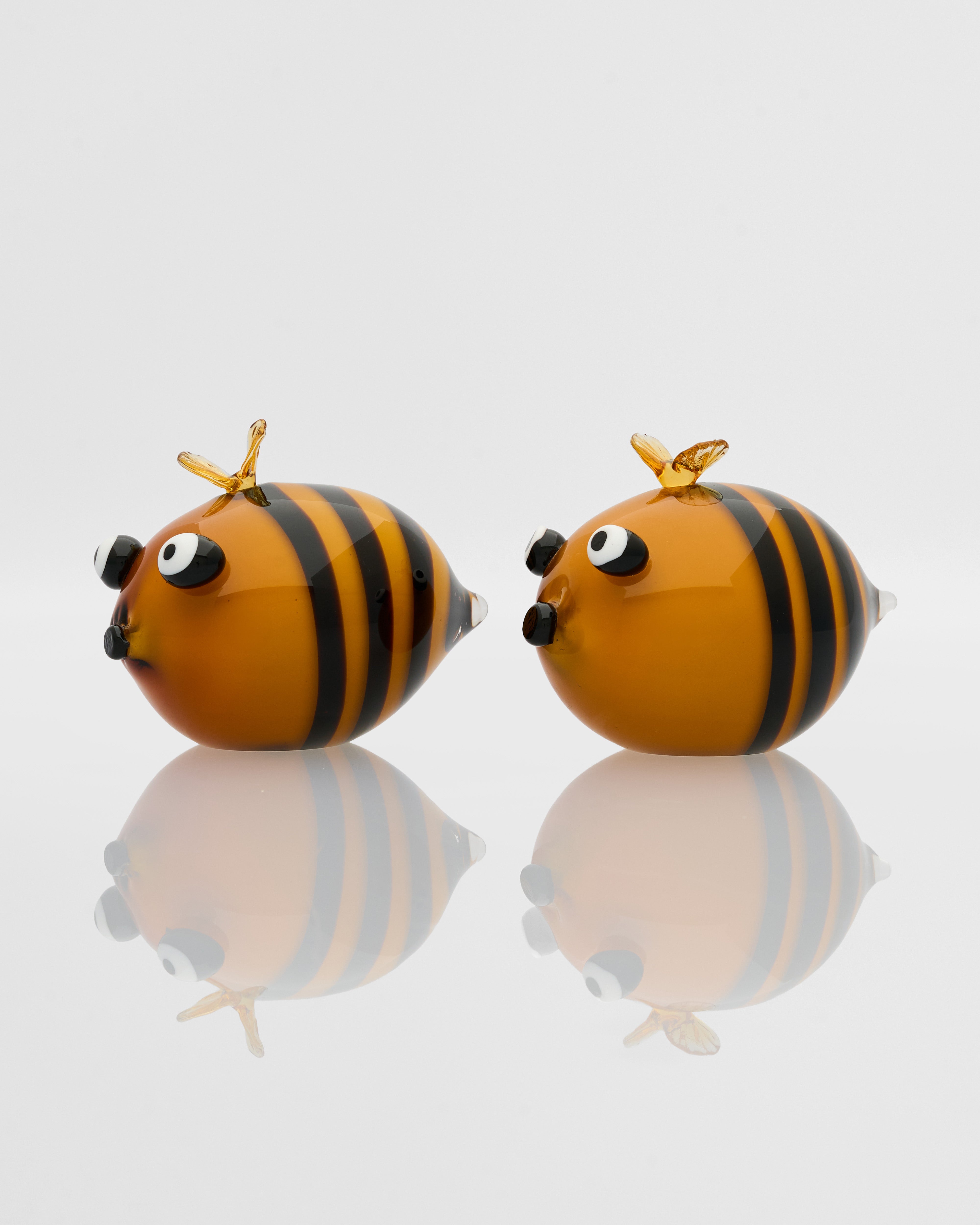 Two glass bee-shaped objects on a reflective surface with a light gray background