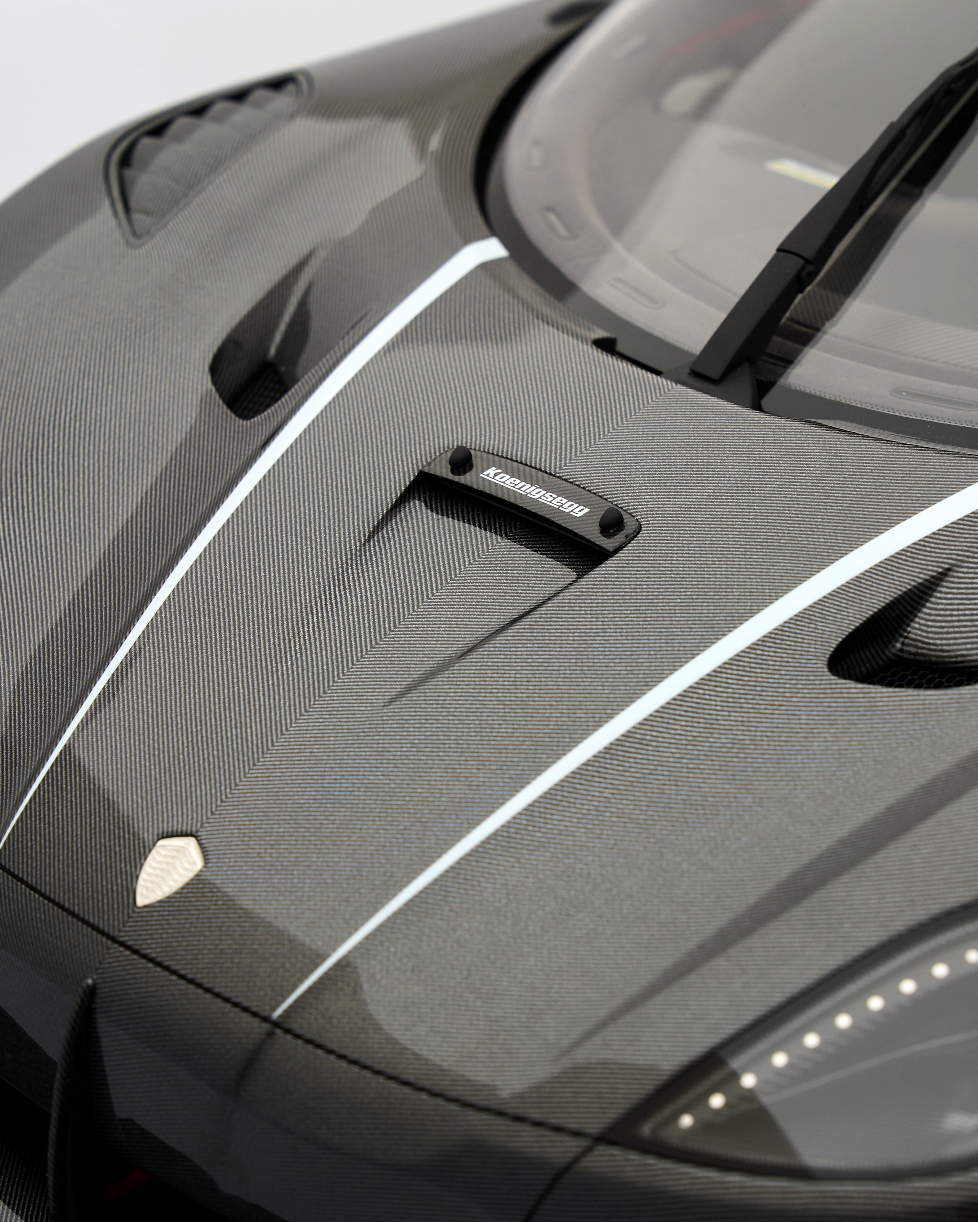 Close-up of a car's carbon fiber hood with a visible brand logo.