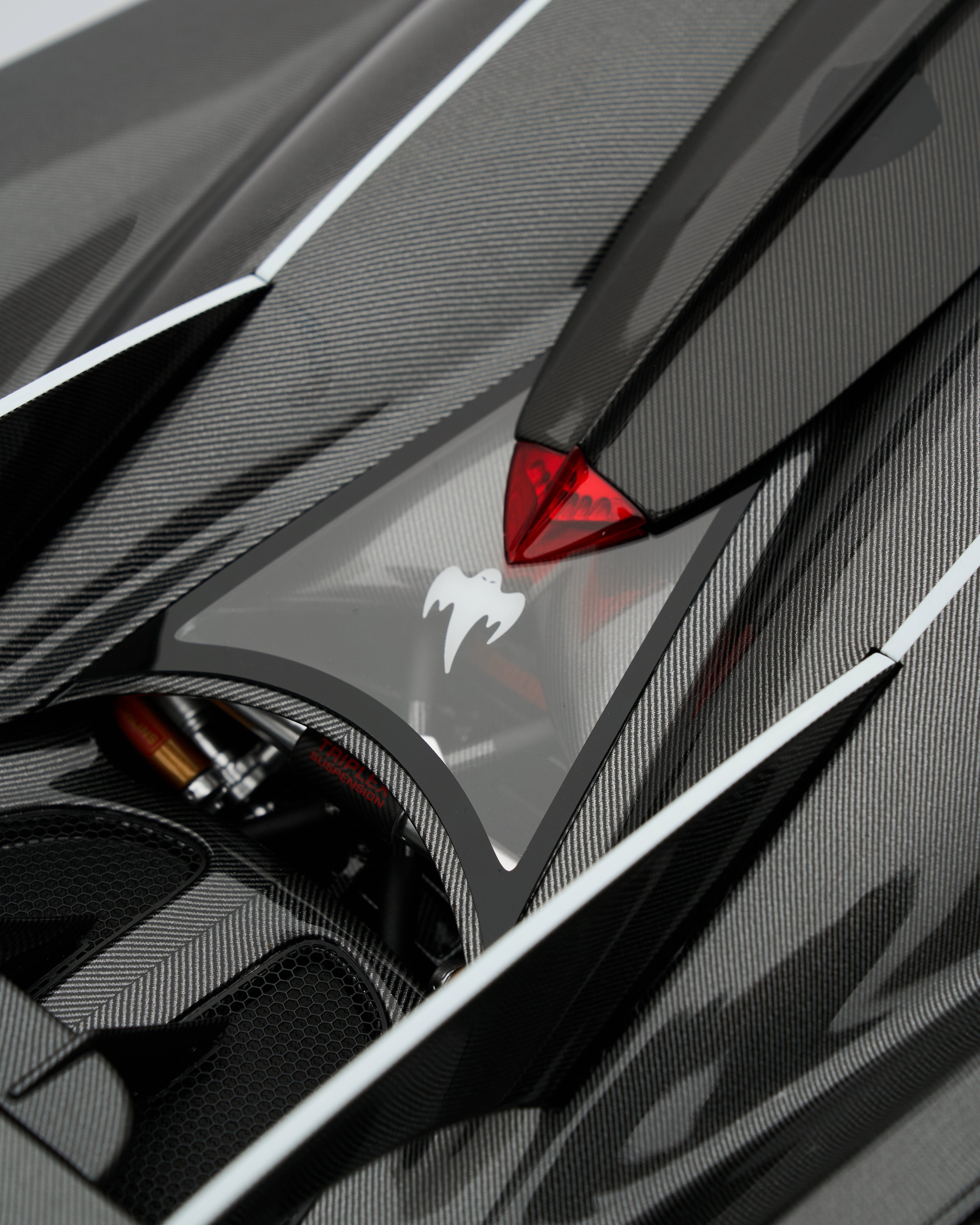 Close-up of a car's carbon fiber panel with a red and white logo.