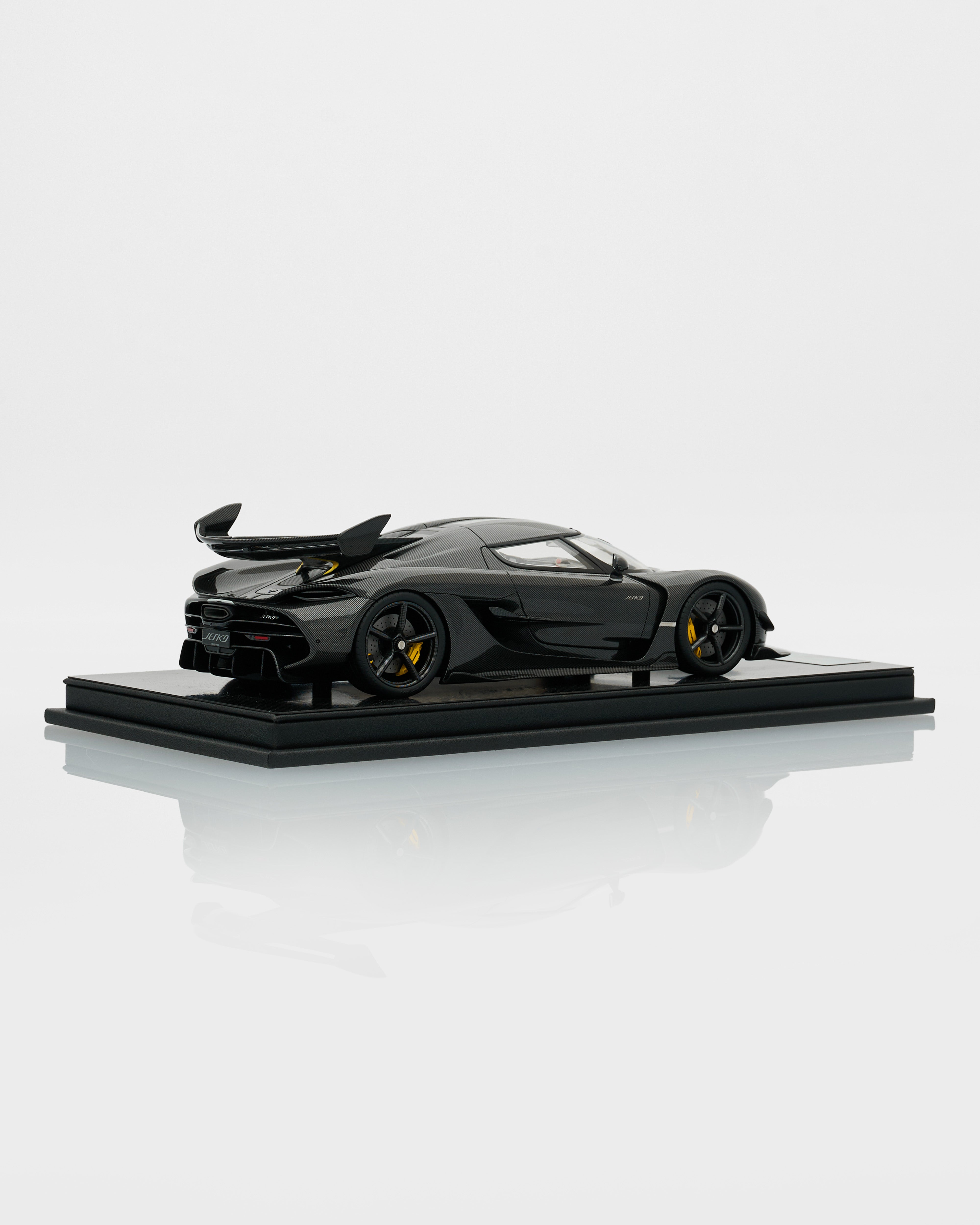 Black sports car model on a reflective platform with a white background