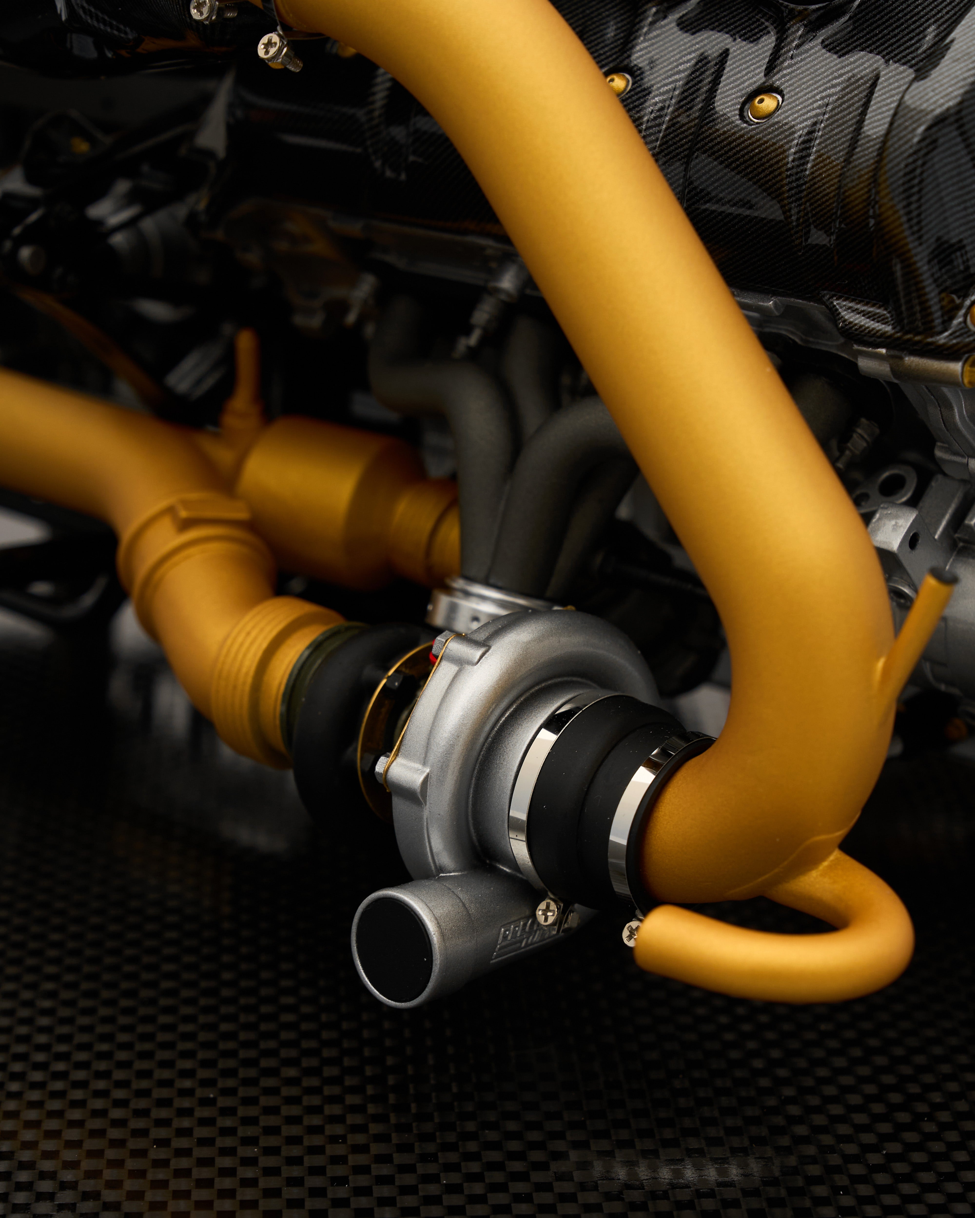 Close-up of a turbocharger with yellow piping on a textured black background