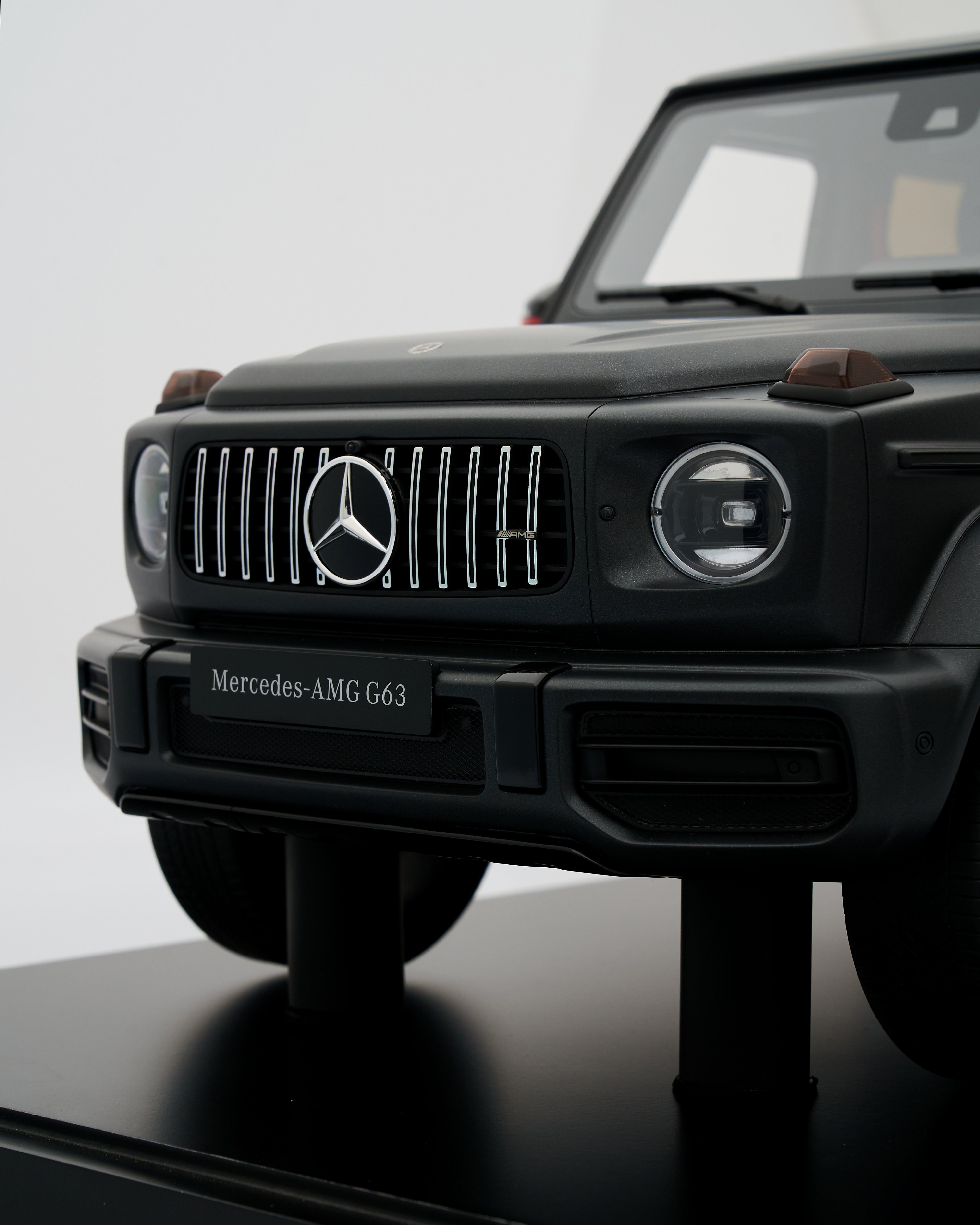 Black Mercedes-AMG G63 model car on a reflective surface with a light gray background