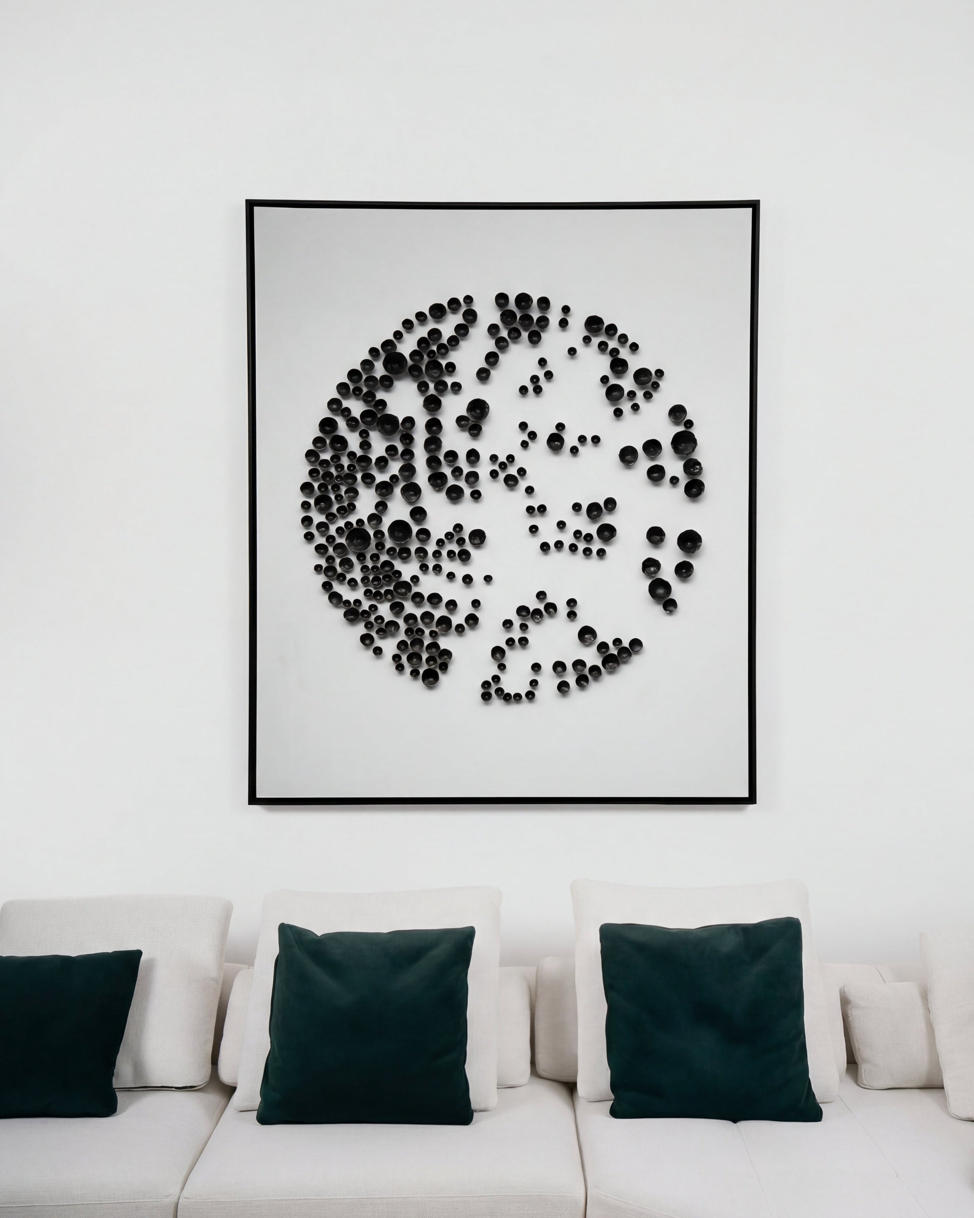 Framed abstract art piece on a wall above a white sofa with green cushions.