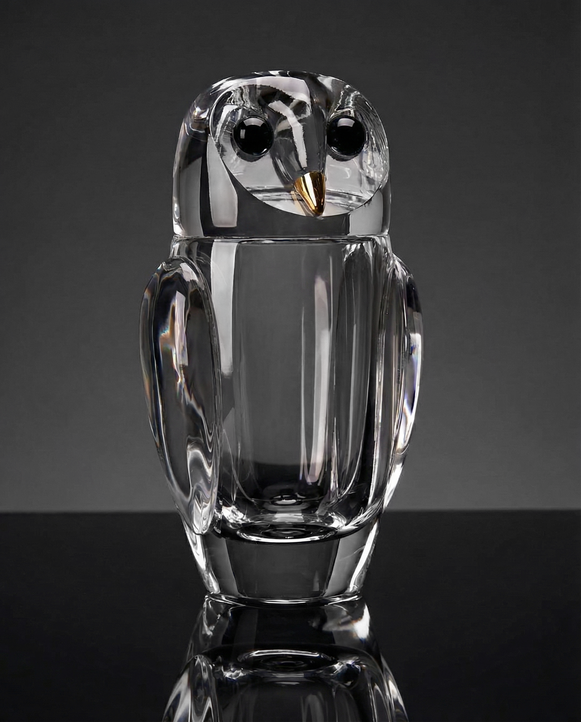 Clear glass owl figurine on a reflective surface with a dark background