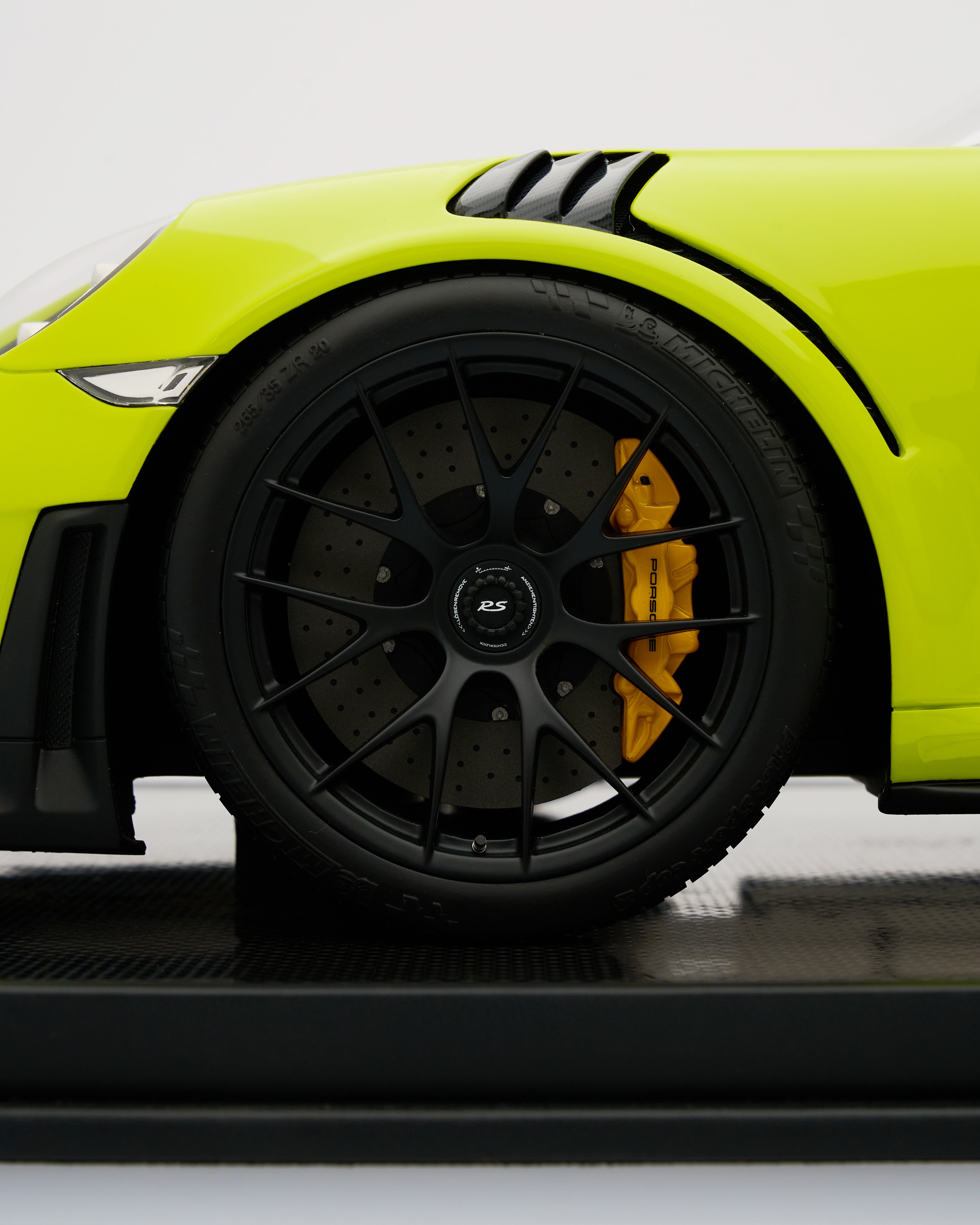 Close-up of a lime green sports car with black rims and yellow brake calipers on a white background