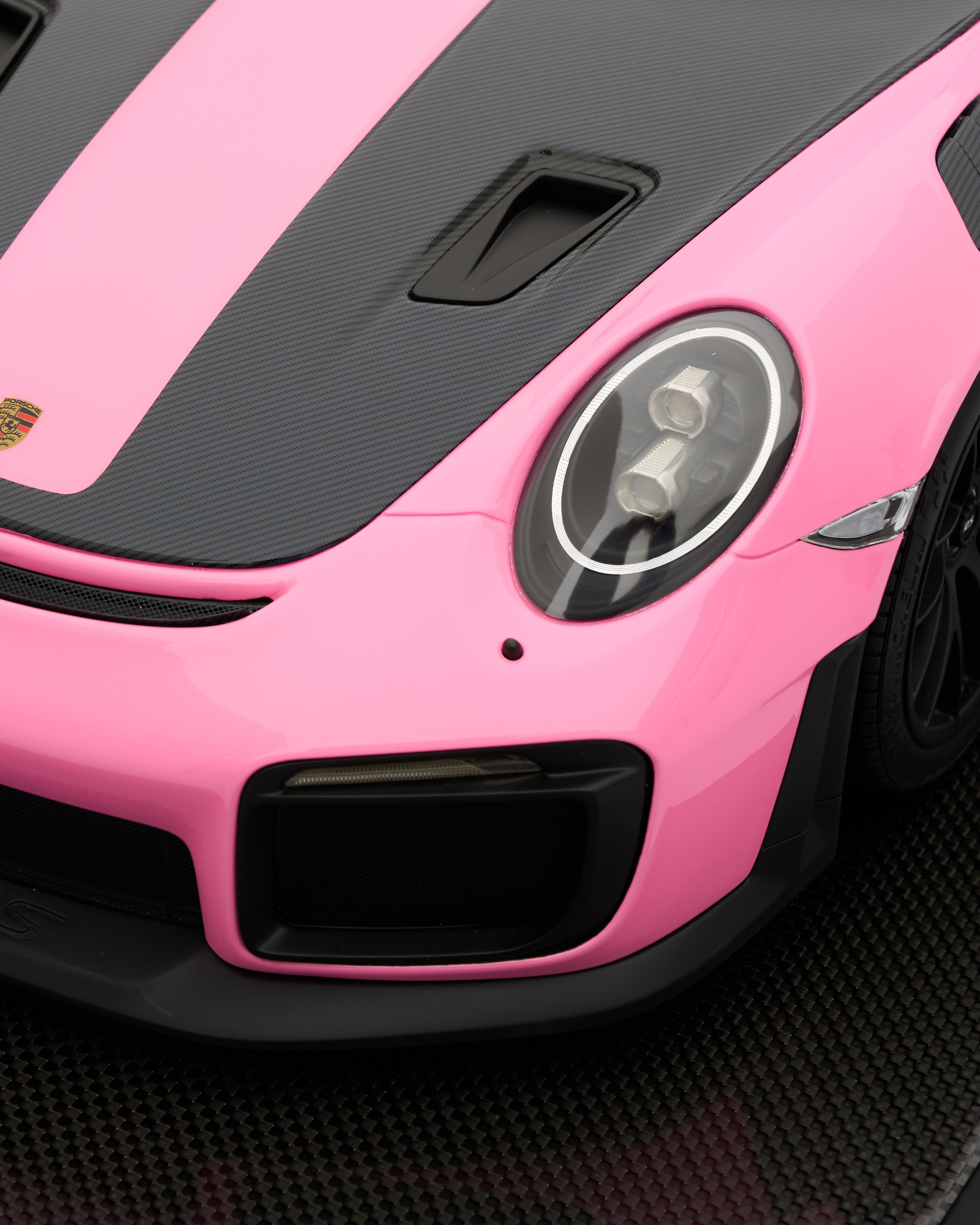 Close-up of a pink and black sports car with a visible Porsche logo.