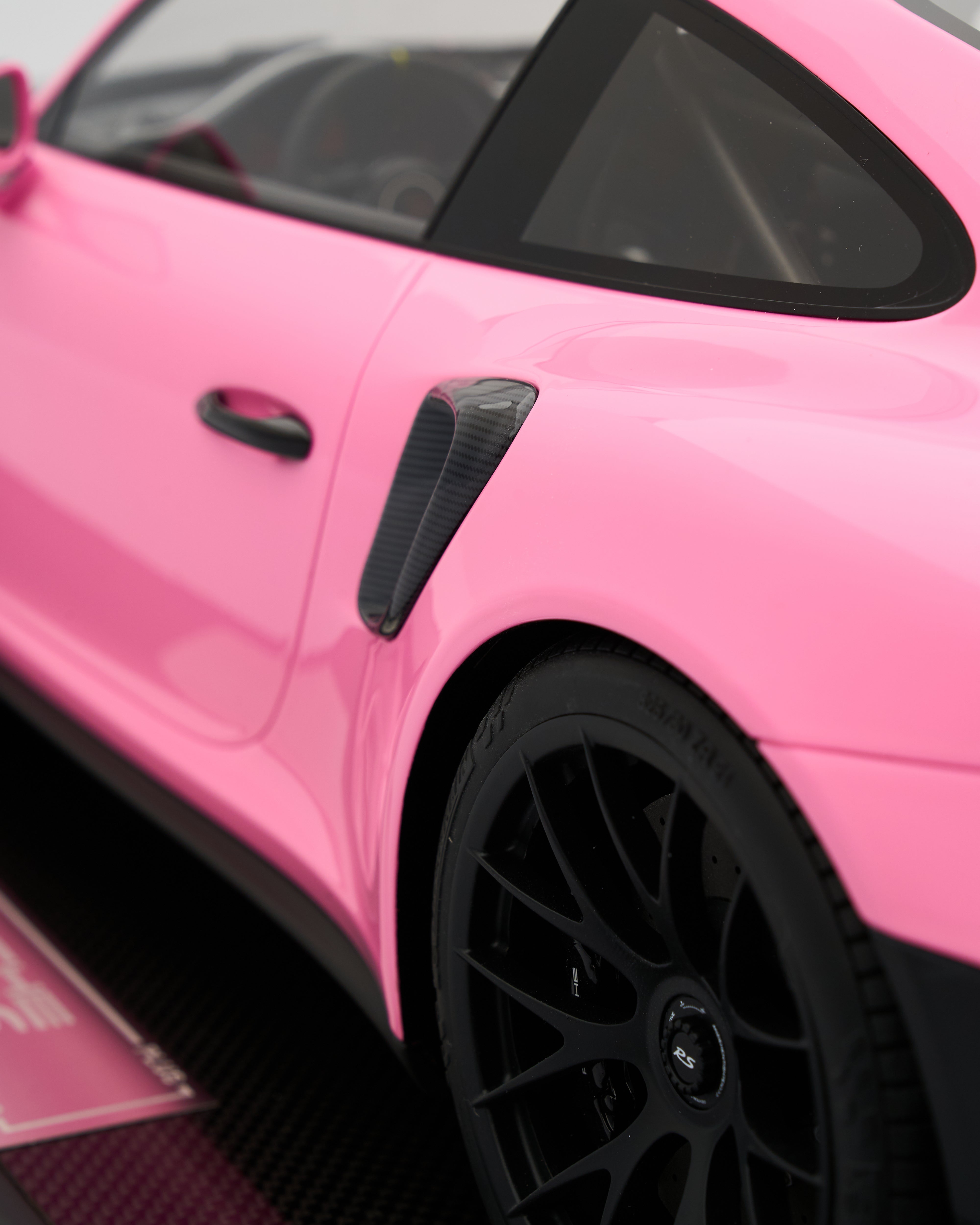 Close-up of a pink sports car with black wheels and carbon fiber accents.