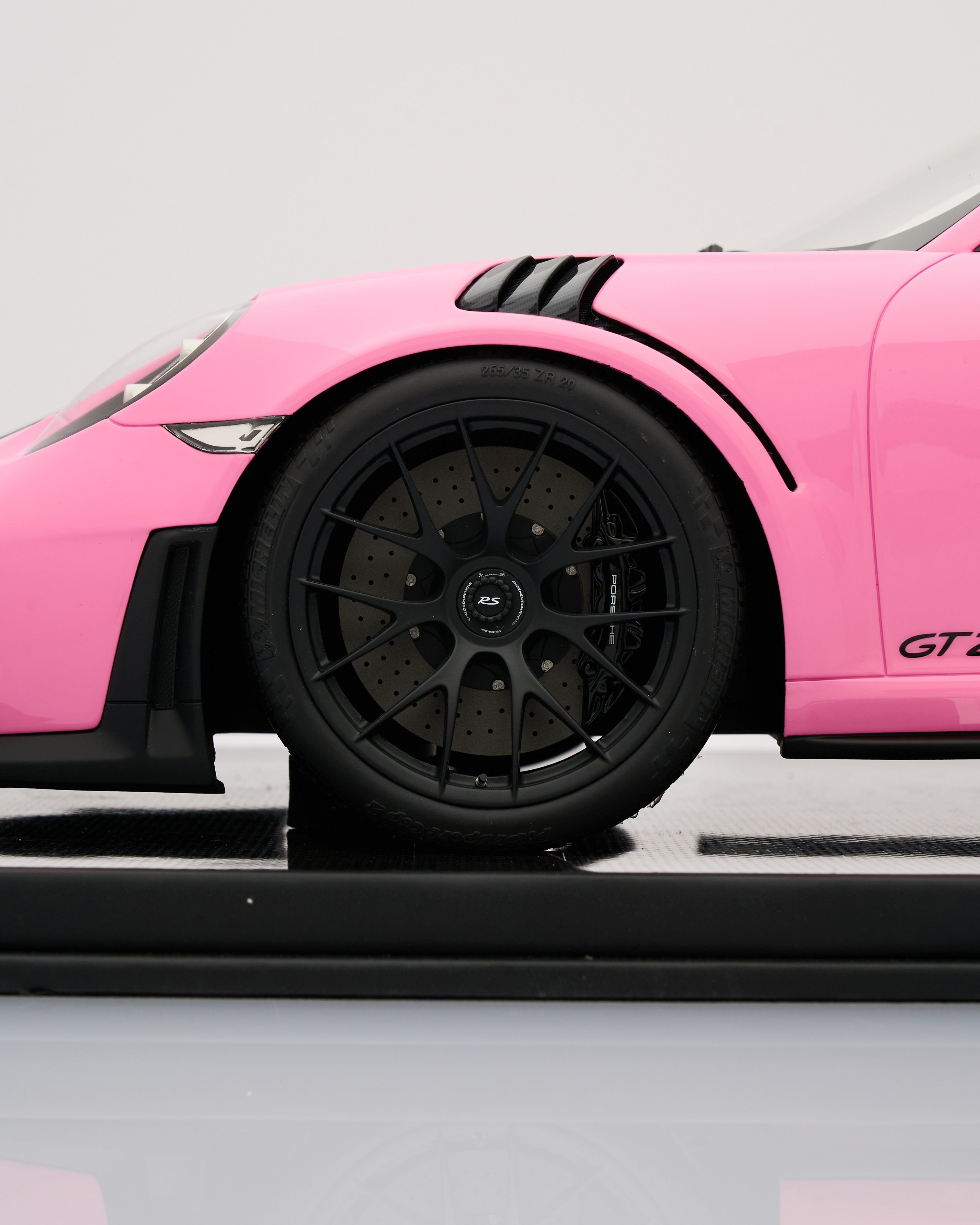 Close-up of a pink sports car with a black wheel on a gray background
