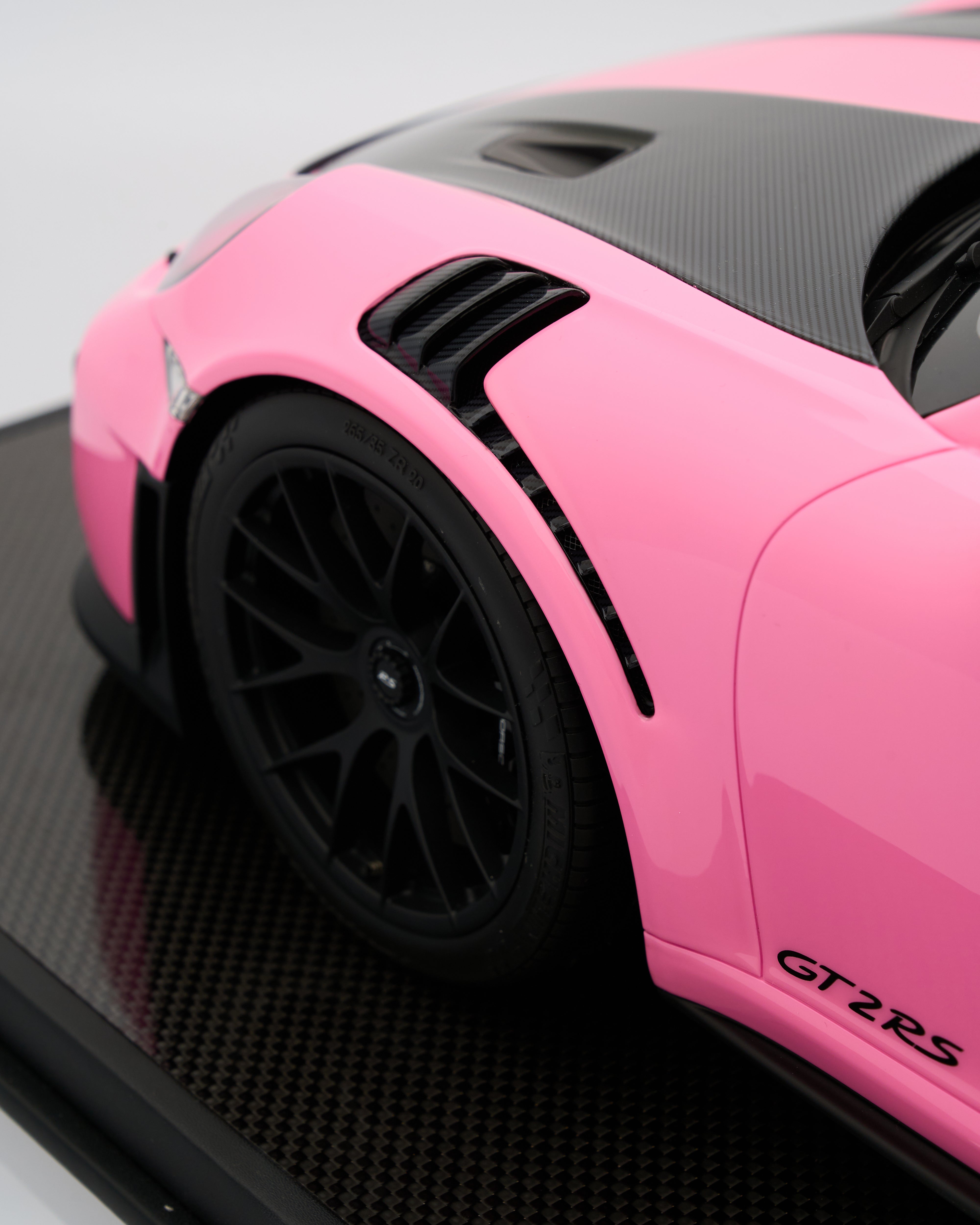 Pink sports car model with black wheels on a reflective surface