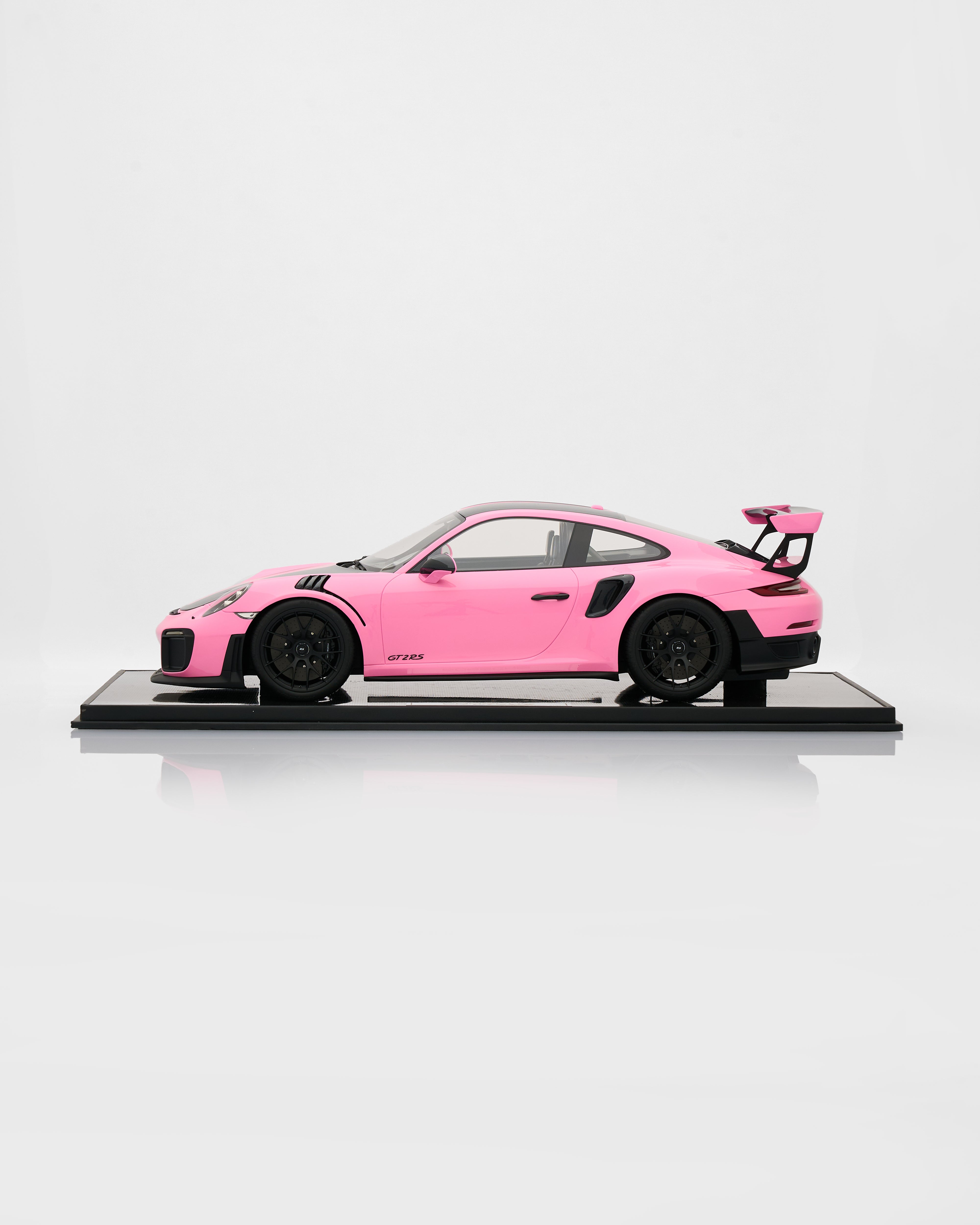 Pink model car on a black platform with a white background