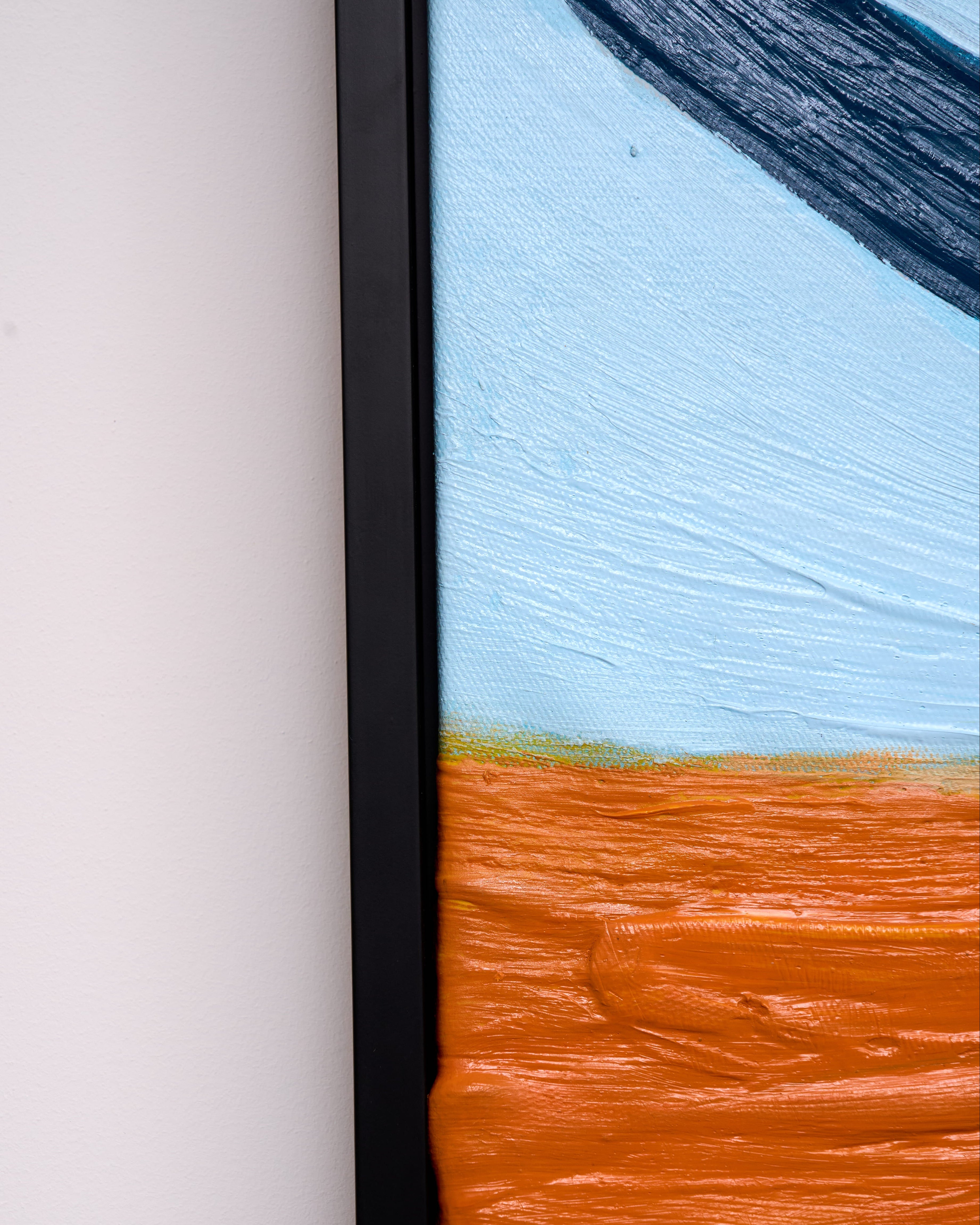 Close-up of a framed abstract painting showing a textured orange lower section, a pale blue upper section, and a dark brushstroke at the top, set against a white wall.
