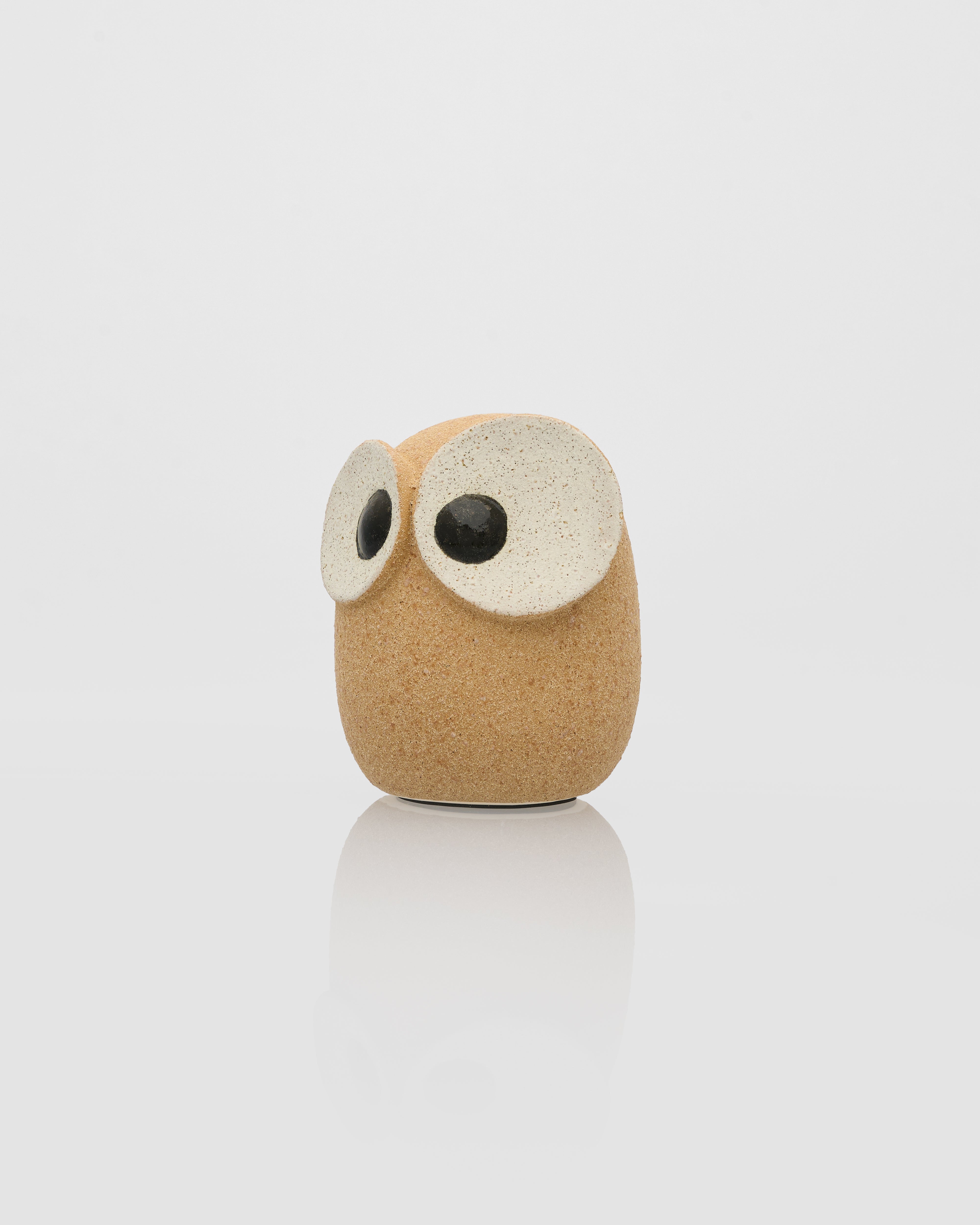 Cylindrical owl-shaped object with a beige body and white face on a light gray background