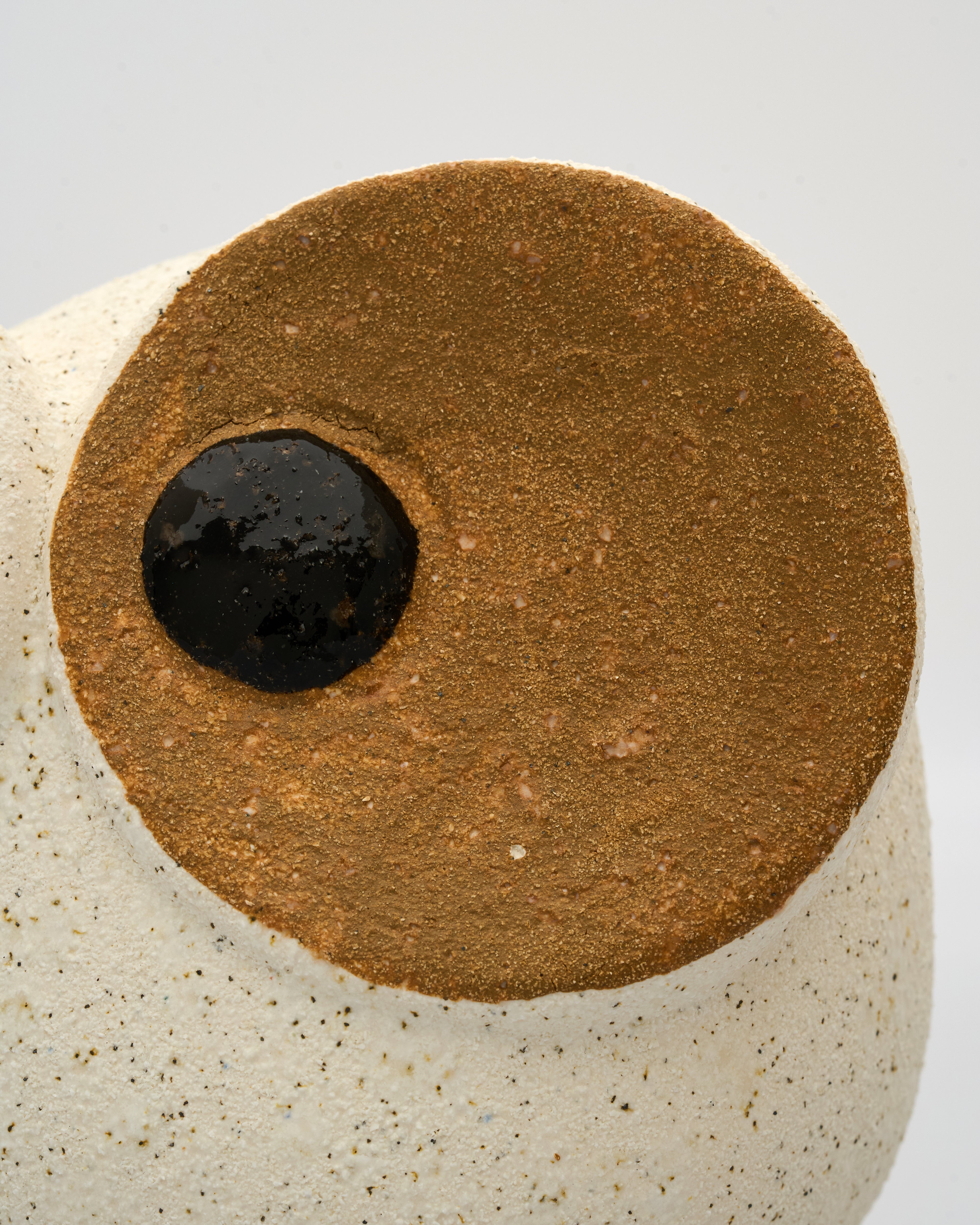 Close-up of a ceramic piece with a brown circular design and black center on a white background