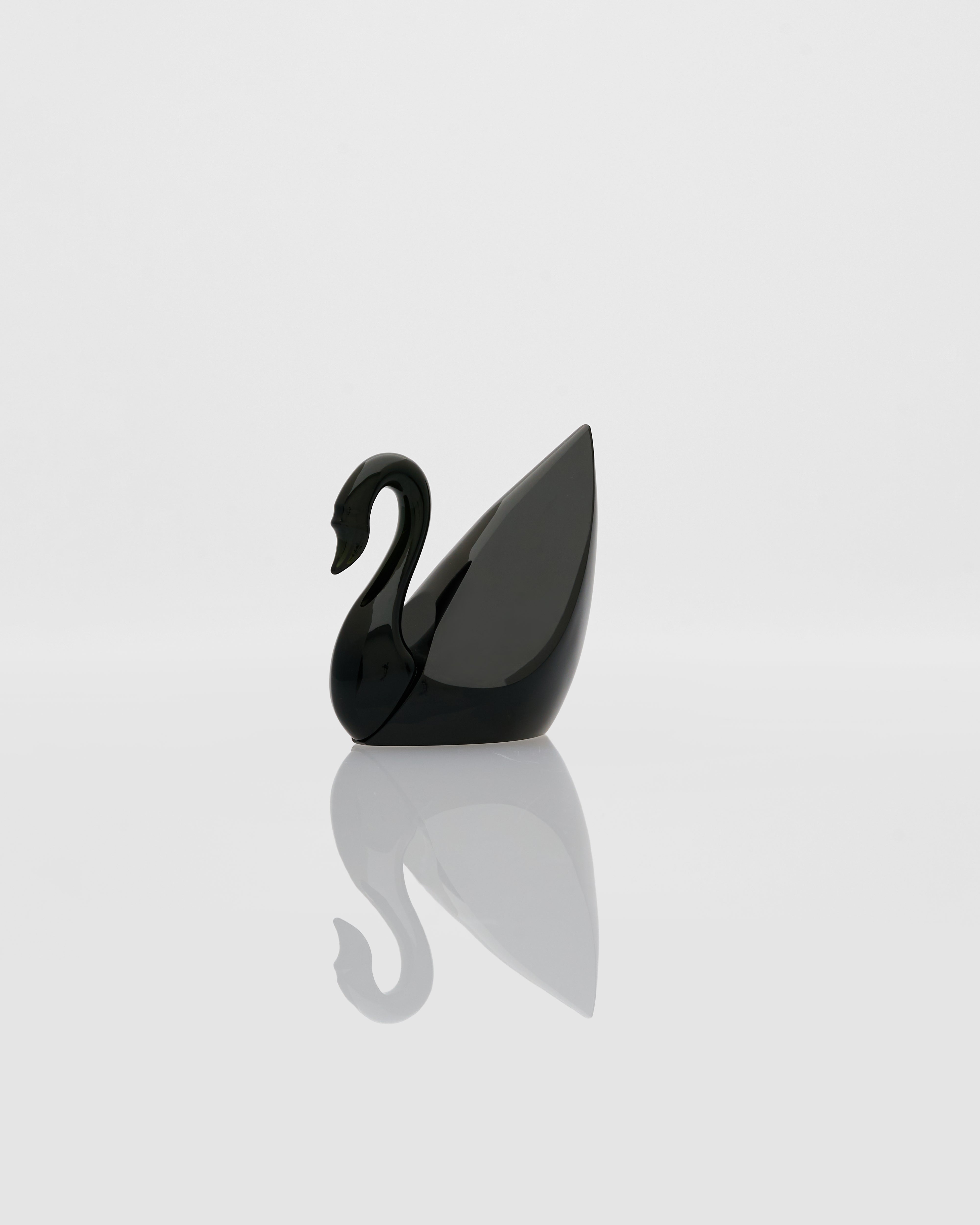 Black swan-shaped object on a reflective surface with a light gray background